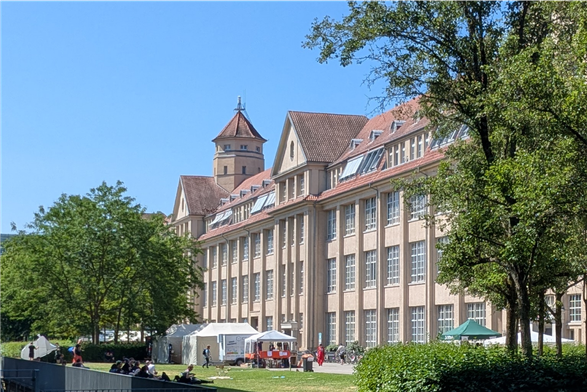 Fassade des ZKM, Längsseite. Blauer Himmel, davor etwas Rasen, weiße Zelte, Hecken und einzelne Bäume.