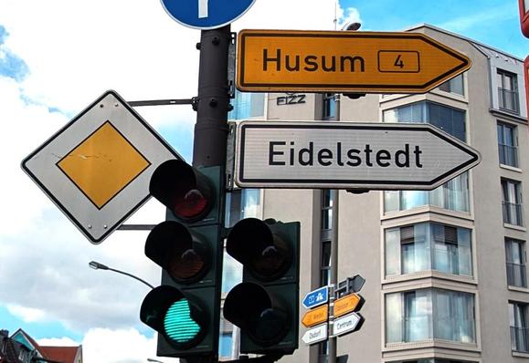 Grüne Ampel mit verschiedenen Verkehrsschildern, u.a Vorfahrtsschild, Wegweiser nach Husum und Eidelstedt