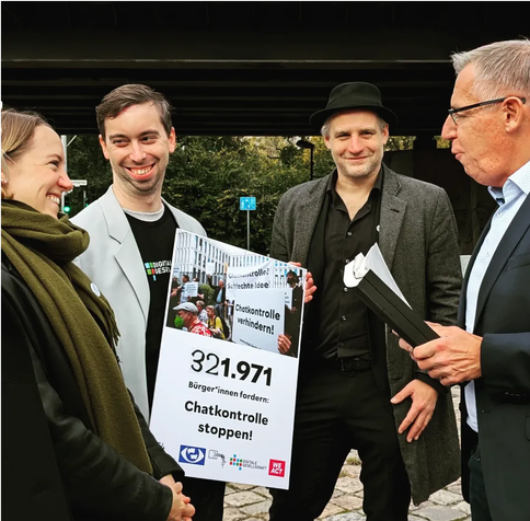 Svea Windwehr, Konstantin Macher und Tom Jennissen übergeben einem Vertreter des Innenministeriums die Petition. Dabei wird ein Plakat gehalten, auf dem die Zahl 321.971 zu erkennen ist, außerdem 'Chatkontrolle stoppen' und einige Logos.