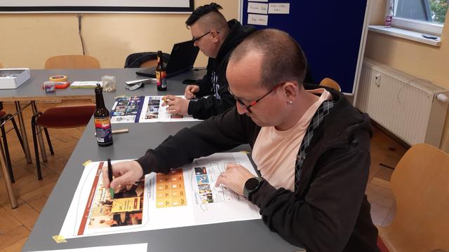 Zwei Menschen sitzen in einem Seminarraum vor jeweils einem Ausdruck von Internetseiten. Mit Filzstiften haben sie unterschiedliche Bereiche eingekreist oder durchgestrichen.