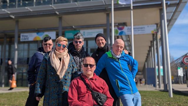 Sechs gut gelaunte Personen vor einem Gebäude. Manche tragen Sonnenbrillen.