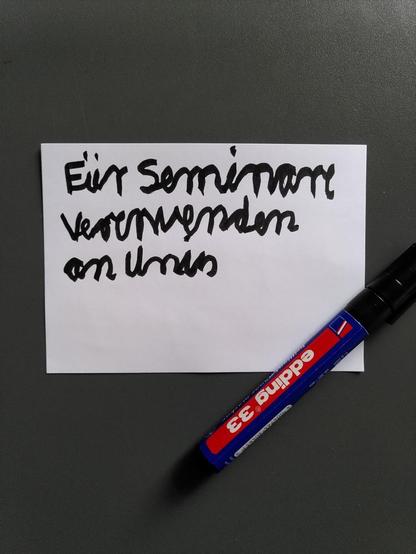 Auf eine weiße Moderationskarte hat jemand in wackeliger Handschrift "Für Seminare verwenden an Unis" geschrieben. Es ist nicht ganz leicht zu lesen. Neben der Karte liegt ein Edding.